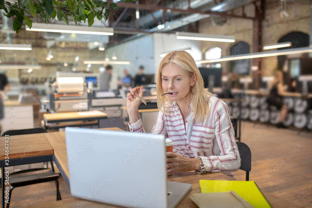 Blonde woman working at laptop, biting glasses temple Blonde woman working at laptop, biting glasses temple