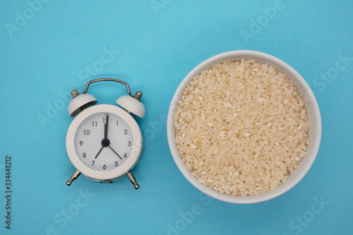 Top view of rice in bowl and clock for healthy food in timing at morning