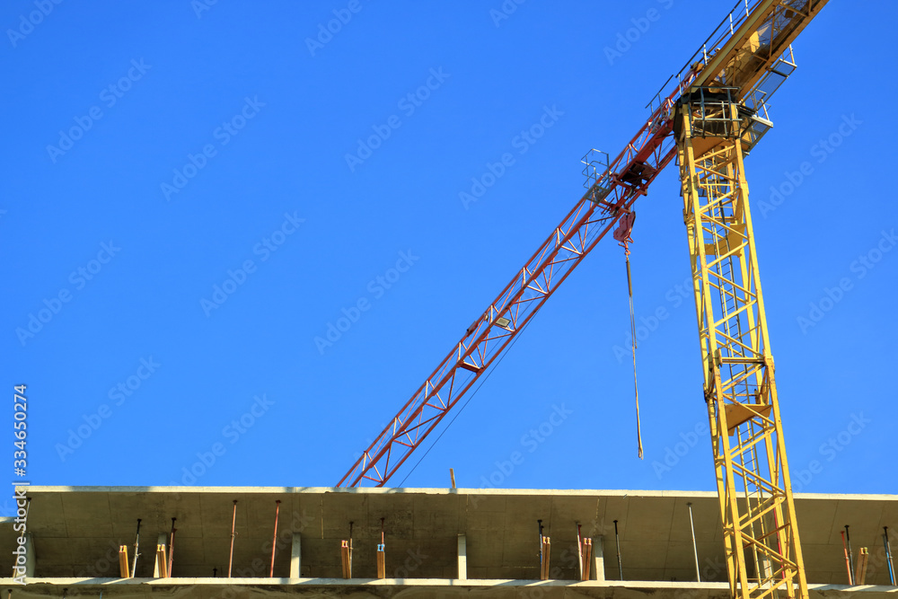 An image of a tower crane against the background of a house under construction.