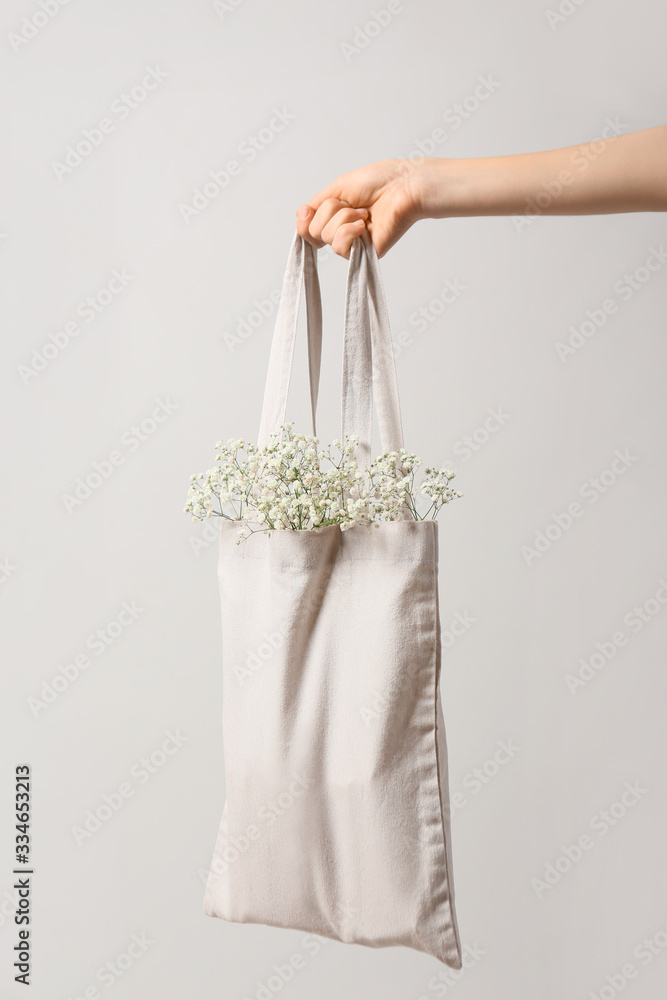 Female hand with flowers in eco bag on light background Female hand with flowers in eco bag on light background