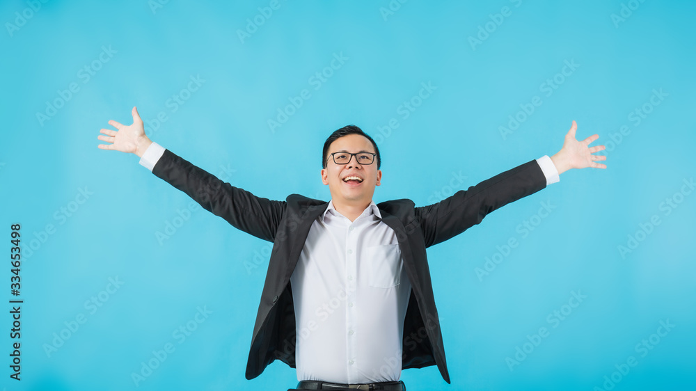 Young Asian businessman wearing glasses rise hand up and feeling happy about his business success idea isolated on blue background.Concept of success creative startup business. Young Asian businessman wearing glasses rise hand up and feeling happy about his business success idea isolated on blue background.Concept of success creative startup business.