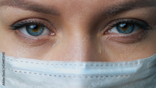 A female doctor therapist in a white robe, mask and gloves. Face close-up. The doctor cries and prays. Tears in eyes. Pandemic and virus epidemic. Coronavirus covid-19.