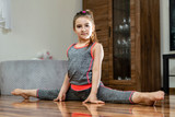 Trening domowy. Mała dziewczynka wykonuje ćwiczenia gimnastyczne na podłodze w salonie.