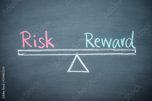Text word risk and reward balance on seesaw drawing writing on chalkboard or blackboard background. Concept of risk and reward analysis in business, financial and investment. 