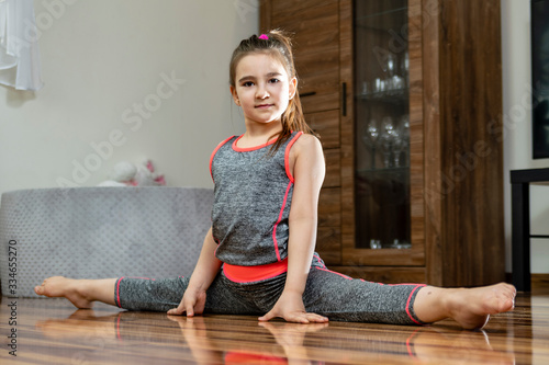 Trening domowy. Mała dziewczynka wykonuje ćwiczenia gimnastyczne na podłodze w salonie.