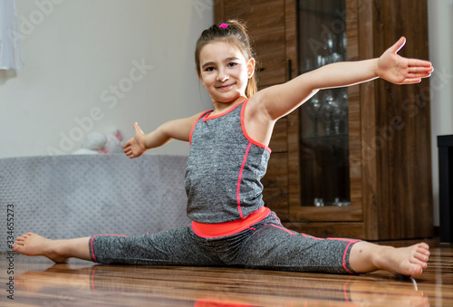 Siad rozkroczny - trening dzieci w domu. Stretching i rozciąganie. Dziewczyna ćwiczy na podłodze w salonie.