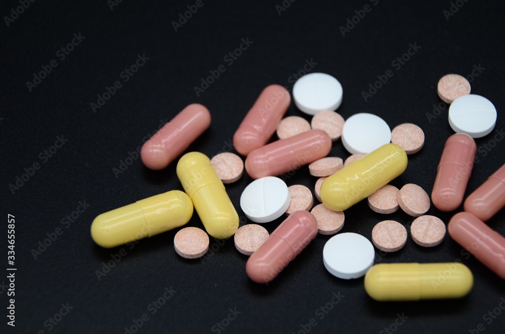 white and pink tablets and pink and yellow capsules on a black background. Coronavirus Covid-19. Copyspace. world pharmaceutical day white and pink tablets and pink and yellow capsules on a black background. Coronavirus Covid-19. Copyspace. world pharmaceutical day