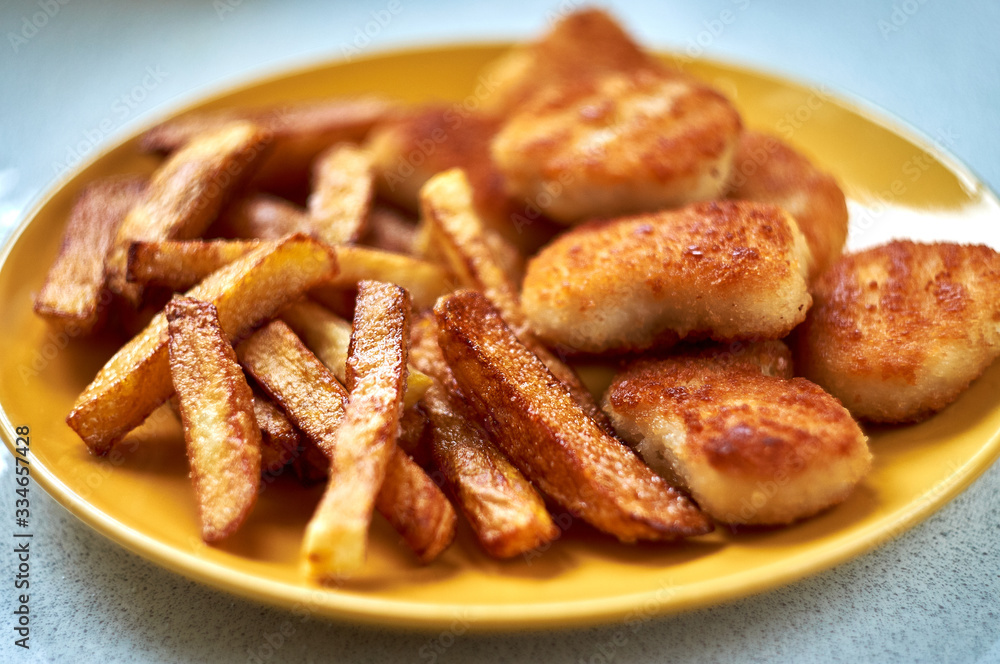 Tasty homemade potato french fries with chiken nuggets on yellow dish Tasty homemade potato french fries with chiken nuggets on yellow dish
