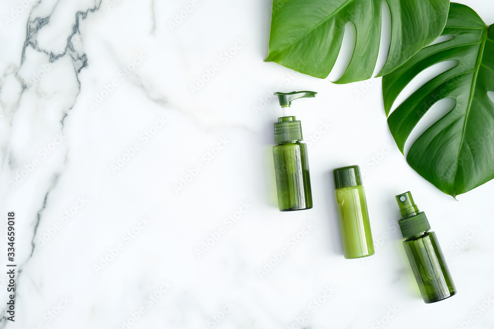 Green cosmetic bottles with monstera tropical plant leaves on marble background. Flat lay, top view, copy space. Natural organic products, beauty treatment and SPA concept Green cosmetic bottles with monstera tropical plant leaves on marble background. Flat lay, top view, copy space. Natural organic products, beauty treatment and SPA concept