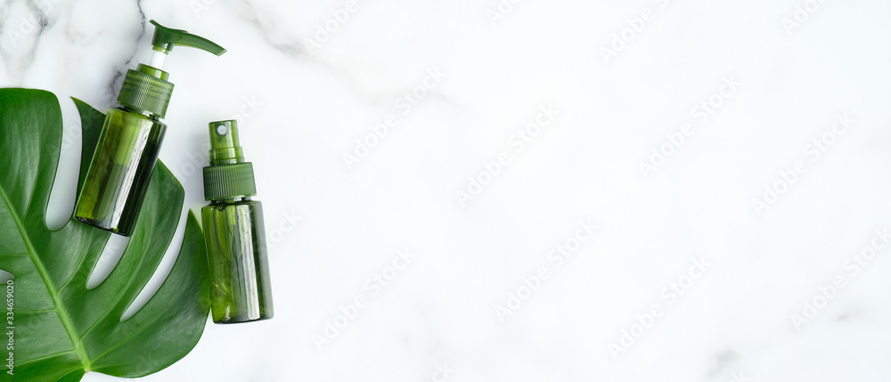 Green cosmetic bottles with monstera tropical plant leaf on marble background. Flat lay, top view, copy space. Natural organic products, beauty and SPA concept Green cosmetic bottles with monstera tropical plant leaf on marble background. Flat lay, top view, copy space. Natural organic products, beauty and SPA concept
