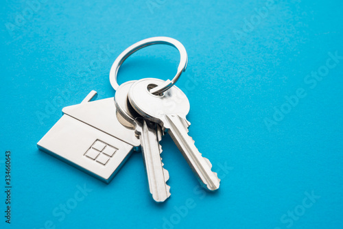 Silver house key with house keychain on blue background with copy space. Dream new house buying, real estate property business concept. © pla2na