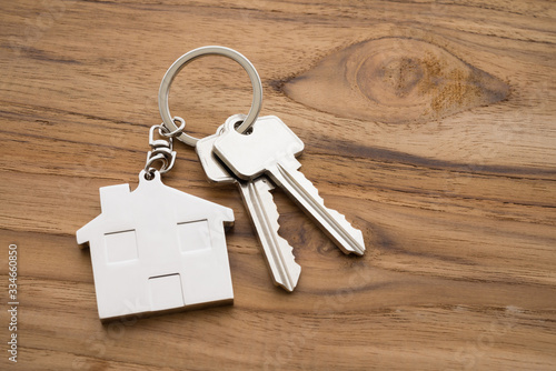 Silver house key with house keychain on wooden background with copy space. Dream new house buying, real estate property business concept.