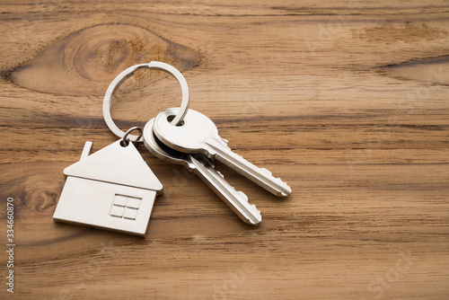 Silver house key with house keychain on wooden background with copy space. Dream new house buying, real estate property business concept.