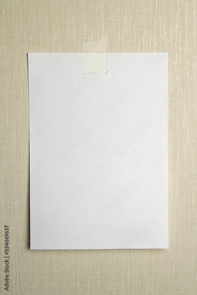 A4 white sheet of paper hanging on a wall glued with a piece of paper tape on a light background. A4 white sheet of paper hanging on a wall glued with a piece of paper tape on a light background.