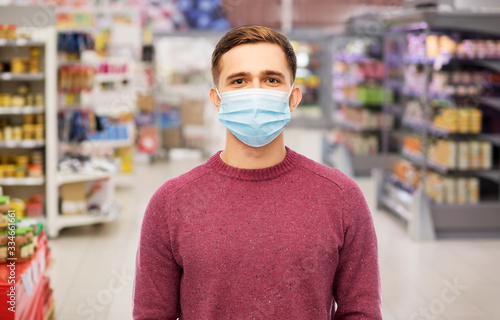 health, safety and pandemic concept - young man wearing protective medical mask for protection from virus over supermarket background