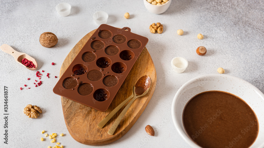 Making chocolate candies in mold and bowl with melted chocolate on light background. Homemade candies. Side view Making chocolate candies in mold and bowl with melted chocolate on light background. Homemade candies. Side view