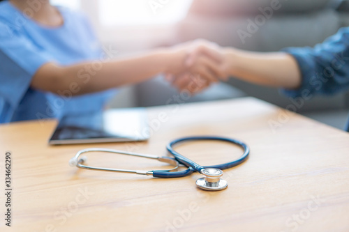 close up showing a stethoscope on table with tablet device and background of female doctor shaking the patients hand in greeting, goodbye and thankful for doctor looking after the patient in comfort