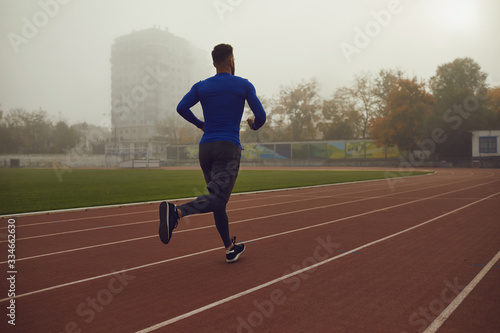 A young athlete runs on a stadium in the fog.