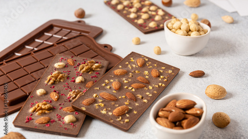 Handmade milk chocolate bars with nuts and dried fruits with molds and ingredients on white background. Side view, close up.