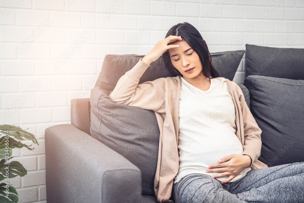 beautiful asian pregnant woman feeling stress from high pregnancy hormones, headache and morning sickness placing hand on forehead with closed eyes, sitting on sofa relaxing resting in living room beautiful asian pregnant woman feeling stress from high pregnancy hormones, headache and morning sickness placing hand on forehead with closed eyes, sitting on sofa relaxing resting in living room