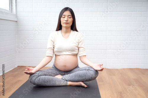 Beautiful asian pregnant woman meditating in accomplished yoga pose on mat training practicing yoga breathing, healthy and fit motherhood feeling happy and strong, pregnancy expecting future new born