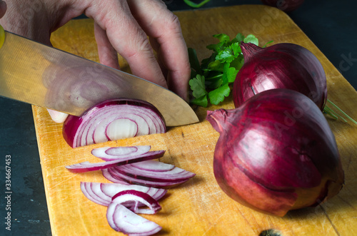 A man cuts red onions on a wooden chopping Board with a kitchen knife. Hands close up. Preparing food. Side view photo