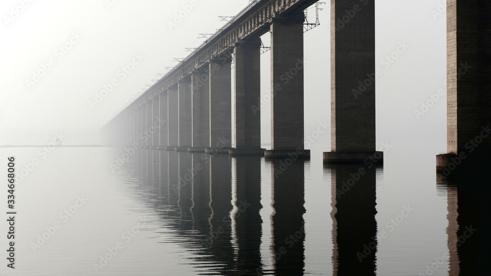 Large transport bridge over river in the morning; strong pillars standing in the water in fog Large transport bridge over river in the morning; strong pillars standing in the water in fog