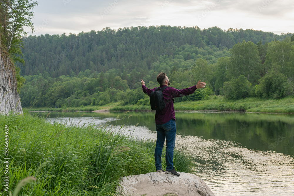 Back view of young man tourist with arms opened wide on bank mountain river. Tourism, hiking, active leisure. Discovering world. Back view of young man tourist with arms opened wide on bank mountain river. Tourism, hiking, active leisure. Discovering world.