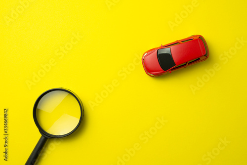 Red car and magnifying glass on yellow background with copy space. Auto insurance business concept. Check car insurance quote for get the best deal. Cover life, property damage, injury of third party