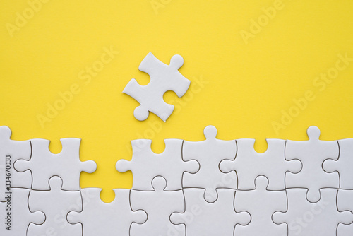Unfinished white jigsaw puzzle on yellow background copy space. Business strategy teamwork and problem solving concept. Teamwork is collaborative effort of team to achieve goal or to complete task