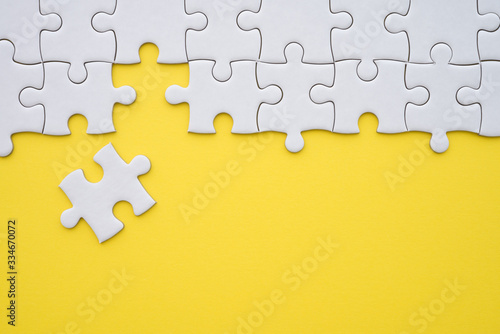 Unfinished white jigsaw puzzle on yellow background copy space. Business strategy teamwork and problem solving concept. Teamwork is collaborative effort of team to achieve goal or to complete task.