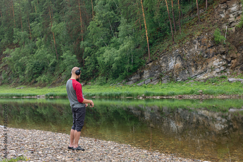 Bearded man with headphones on mountain river bank. tourist, traveler or explorer in his spare time listening to music