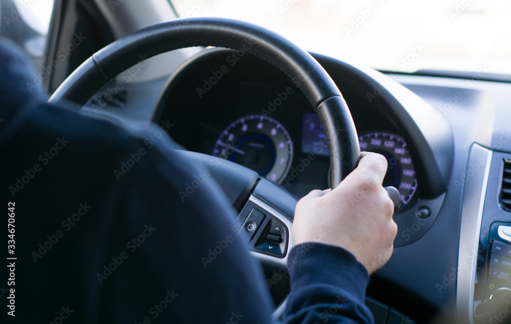 Naklejka premium a young man is sitting at the wheel of a car, hand on the steering wheel. rear view of the dashboard