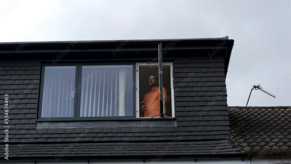 Self Isolation, Man Standing Alone At Attic, Loft Window On Phone In Orange Polo Shirt, Coronavirus, Covid-19 Stay Home March 2020 Self Isolation, Man Standing Alone At Attic, Loft Window On Phone In Orange Polo Shirt, Coronavirus, Covid-19 Stay Home March 2020
