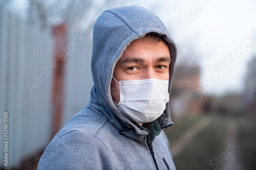 a sad man in jacket hood in medical mask on street