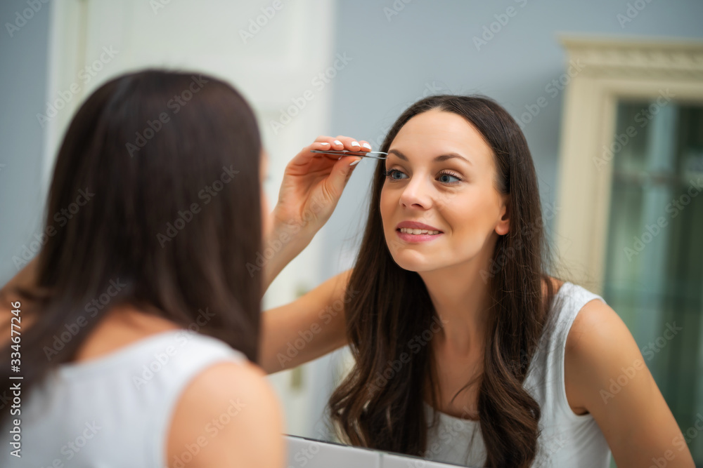 Young woman is plucking eyebrows in bathroom. Young woman is plucking eyebrows in bathroom.