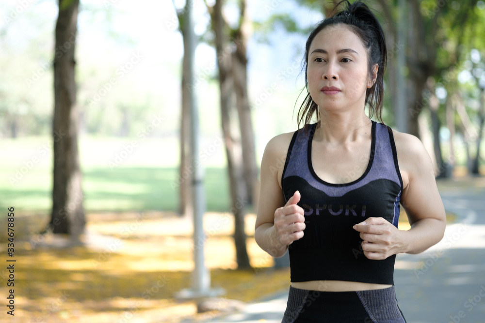 Asian woman wearing black sports bra is exercising by running in public park. Urban health care concept. Asian woman wearing black sports bra is exercising by running in public park. Urban health care concept.