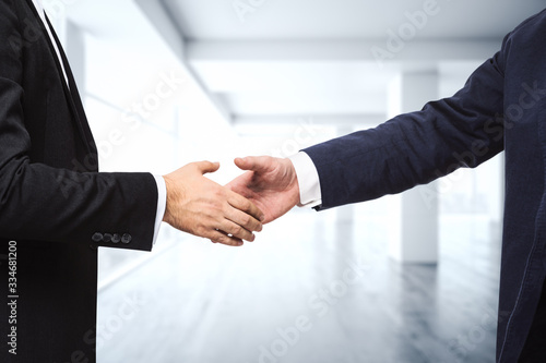 Two businessmen shake hands on the background of empty modern office, signing of a contract concept, close up