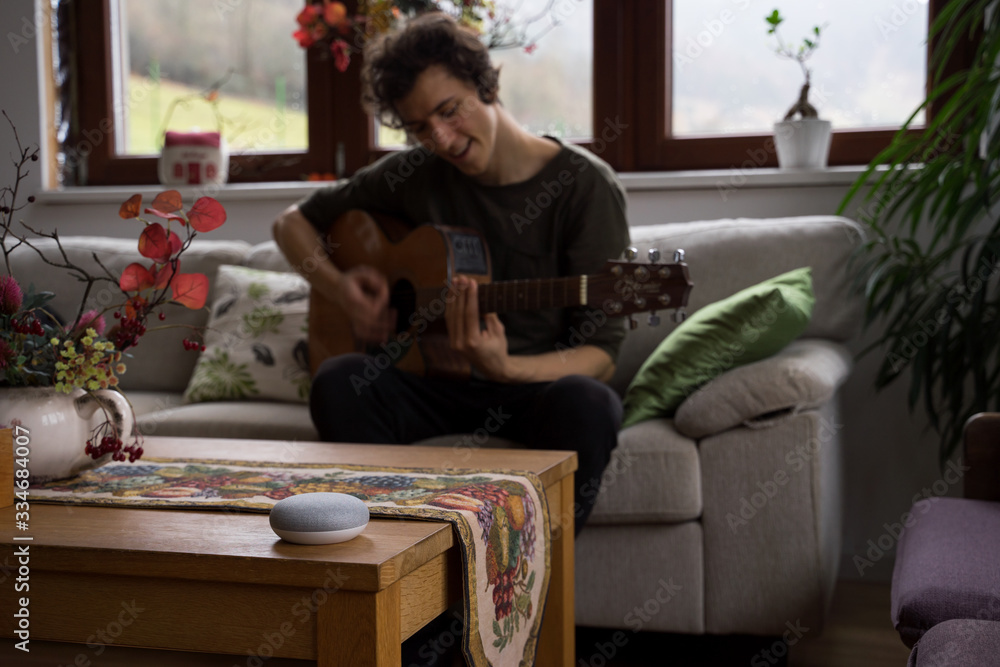 Obraz premium smart home voice activated speaker in home with man on guitar in background. Stay at home.