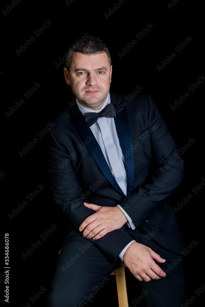 beautiful businessman wearing black suit sitting on black studio background