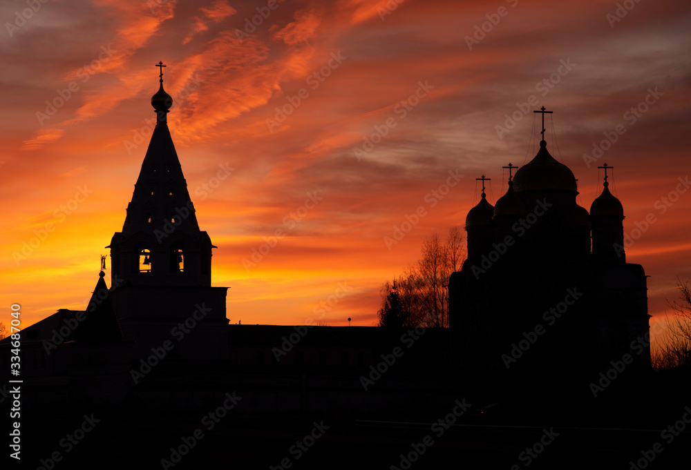 The black silhouette of the monastery against the background of a bright multicolored sunset.