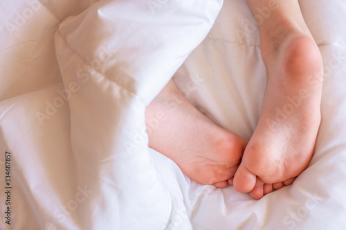 Child feet under the white blanket. Tenderness of morning dream