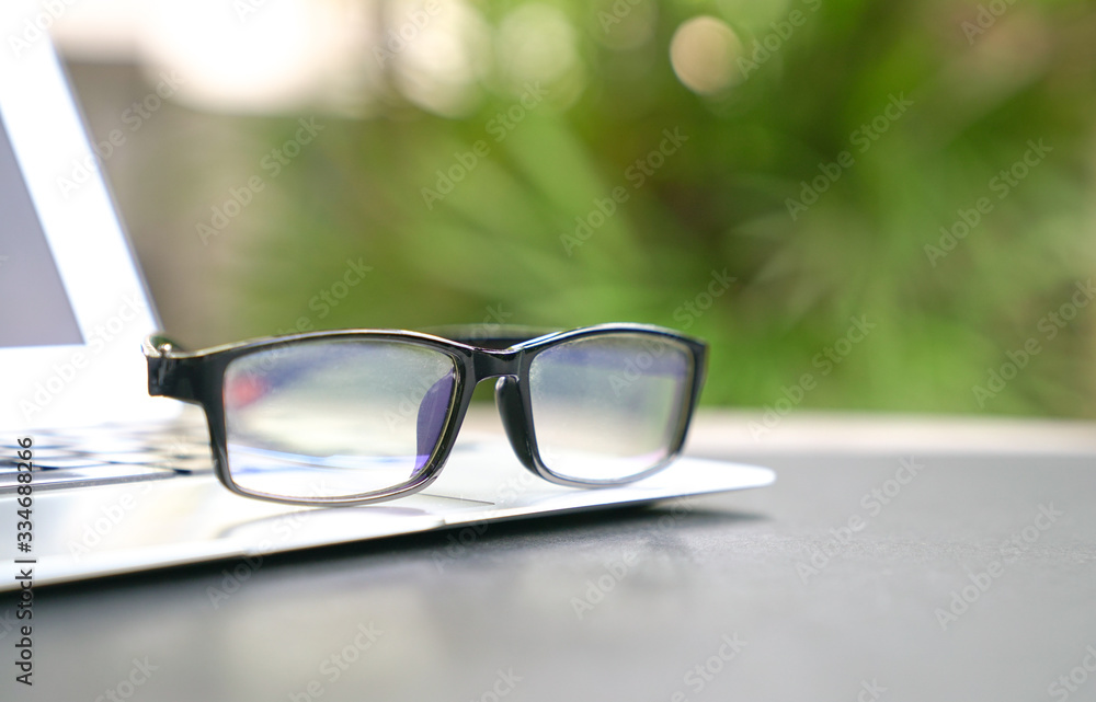 Spectacles on top of computer laptop with home and green nature background. Copy space.