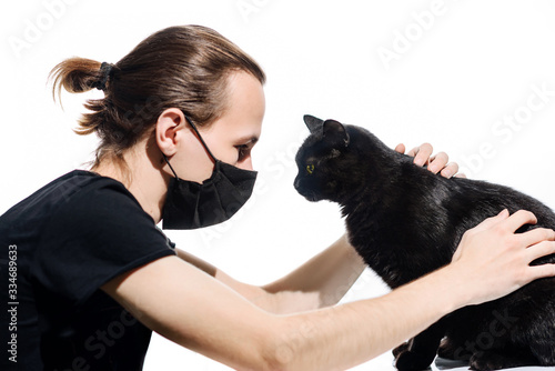 Young man in medical mask holds a black cat  isolated on white background.