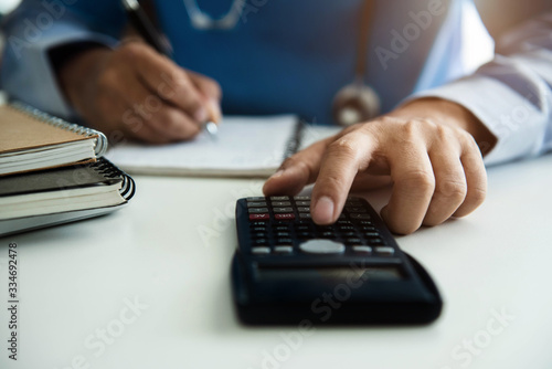 Doctor or accounting department writes a note and uses a calculator to calculate expenses - income. Of hospital staff.
