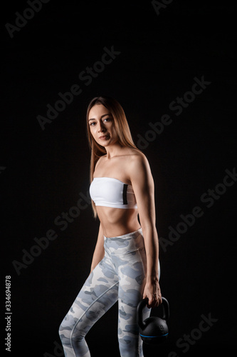 Fitness exercise woman holding kettlebell strength training biceps. Beautiful sweaty fitness instructor looking. Mixed race Caucasian female sweating isolated on black background