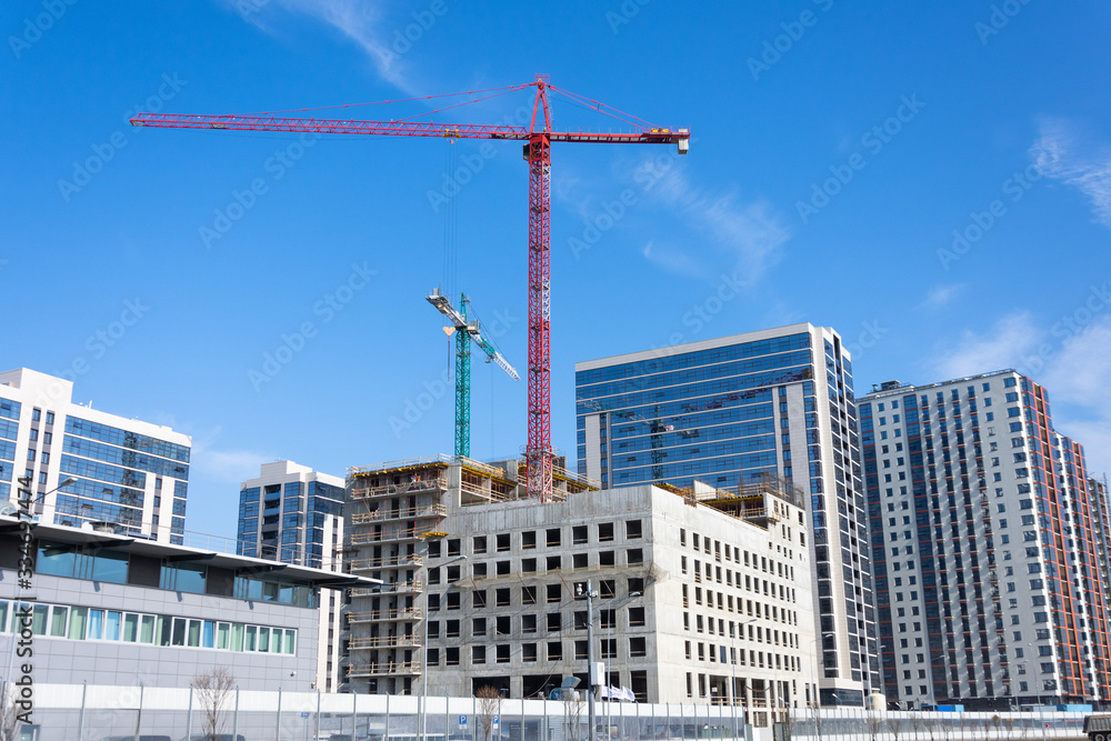 View of a building with high construction cranes and nearby a glass tower, built houses.