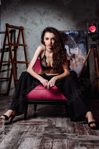 Girl in a Jacket, Pants and Sexy Lingerie Posing in a Studio. Model sensually posing in retro loft interior. curly hair