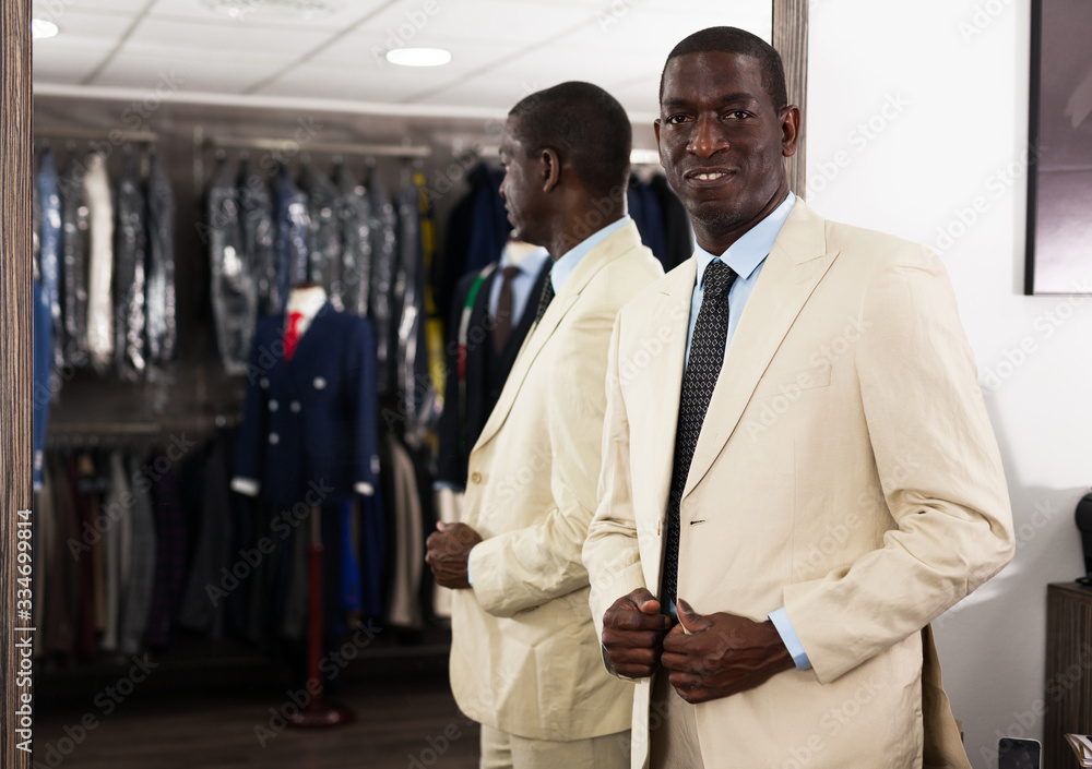 Confident male customer choosing fashion beige suit in mens store