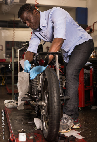 Afro american worker fixing failed motorcycle in workshop